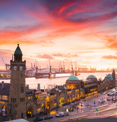 Hamburger Landungsbrücken bei Sonnenuntergang mit Blick auf den Hafen und Kräne im Hintergrund